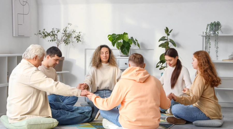 Image of men and women sitting in a circle at a Celebrate Recovery meeting with everyone holding hands - Celebrate Recovery principles faith-based addiction recovery and spiritual growth